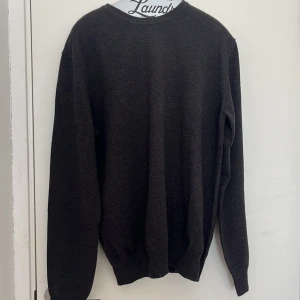 Mörkgrå tröja från Litoral Copenhagen - Mörkgrå långärmad tröja från Litoral Copenhagen i mjuk cashwool. Klassisk rak passform med ribbade muddar vid ärmslut och nederkant. Perfekt för dig som gillar stilrena och enkla plagg.