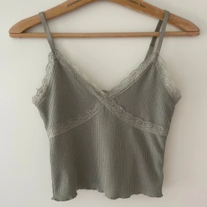 Grönt ribbat linne med spetsdetaljer - Grönt ribbat linne med tunna axelband och fina spetsdetaljer. Den har reglerbara band. Jag vet inte vart den är ifrån men kanske från hm. 