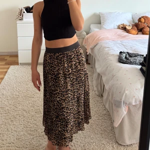 Leopardmönstrad midikjol med resårmidja - Säljer en snygg midikjol med leopardmönster och bred svart resår i midjan. Kjolen har en lätt utställd passform och är gjord i ett mjukt, flowy material.