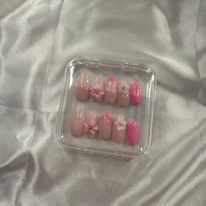 Rosa och nude pres ons  med 3D-blommor - Säljer ett set pres ons i mandelform med nude och rosa färger. Några naglar har handgjorda 3D-blommor i vitt och rosa med små pärldetaljer. Perfekt för dig som vill ha en söt och trendig look.
