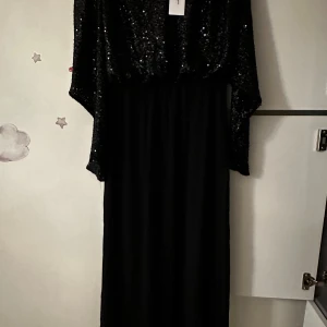 Svart glittrig långklänning från Boohoo - Säljer en svart långklänning från Boohoo med glittrig paljettöverdel och lång ärm. Klänningen har en elegant och festlig look, perfekt för speciella tillfällen. Mjuk kjol i svart tyg och rund halsringning.