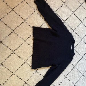 Svart stickad tröja från C - Mysig svart stickad tröja från C i storlek 146/152. Tröjan har rund halsringning, långa ärmar och bred ribbstickning vid ärmslut och nederkant. Perfekt för kyligare dagar och enkel att matcha med olika outfits.