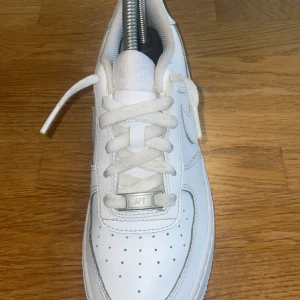 Vita Nike Air Force 1 sneakers - Klassiska helvita Nike Air Force 1 sneakers med snörning och rund tå. Skorna har en platt sula och är tillverkade i skinn med diskreta sömmar och Nike-logga på sidan och hälen.