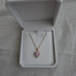 Halsband med hjärthänge och rosa - Halsband med ett hjärtformat hänge i rosa och små gnistrande stenar runt.
