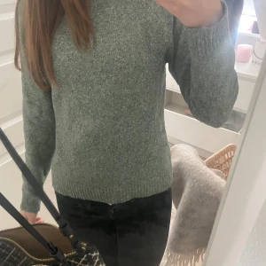 Grön stickad tröja - Mysig grön stickad tröja med rund hals och långa ärmar. Tröjan har en klassisk passform och ribbade muddar vid ärmslut och nederkant. Perfekt för kyligare dagar.