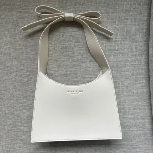 Kate spade väska  - Säljer en stilren vit axelväska från kate spade med bred axelrem och söt rosettdetalj upptill. Gjord i skinn och inköpt för 1000 kr. 