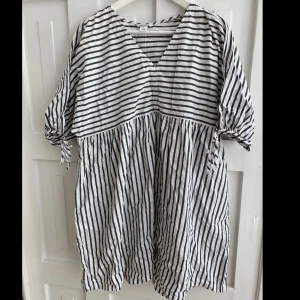 Randig klänning från Monki - Säljer en luftig vit och svart randig klänning från Monki med v-ringning och knyt på ärmarna. Klänningen har en lös passform, perfekt som sommarklänning till stranden!