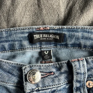 Utra low rise jeans från True Religion - Säljer ett par favorit jeans från True Religion med bootcut-passform då de tyvärr blivit lite för stora för mig. Jeansen har ljusrosa sömmar, stretchigt material och ikoniska bakfickor med broderad logga. Längst ned på jeansen är de lite slitna (se bild), men personligen tycker jag inte att det är något som påverkar helhetsintryck negativt. Nypris 1399