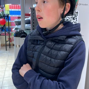 Svart dunväst med dragkedja - Svart dunväst med dragkedja framtill och hög krage. Västen har en sportig look och är perfekt att bära över en hoodie. Passar bra för kyligare dagar och ger en avslappnad stil.