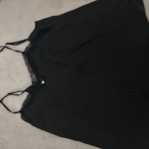 Svart linnetopp med spetsdetaljer - Snabb affär kan pris sänkas. Säljer en svart linnetopp/ nattlinne med tunna axelband och fina spetsdetaljer längs urringningen. Toppen har en mjuk och lätt känsla. 