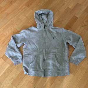 Grå hoodie från Polo Ralph Lauren - Klassisk grå hoodie från Polo Ralph Lauren i storlek XL barn/XS vuxen storlek. Tröjan har en dragkedja. Den är lite urtvättad.