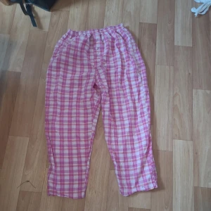 Rosa och vita rutiga pyjamasbyxor - Säljer ett par mysiga pyjamasbyxor i rosa och vitt rutigt mönster. Byxorna har resår i midjan och en knapp framtill. Perfekta för slappa dagar hemma. Lätta och luftiga i bomull. Dom är köpta i Thailand och använda sparsamt, pris är diskuterbart skulle gissa stl s/m