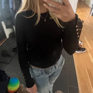 Svart tröja från Zara - Säljer en svart långärmad tröja från Zara med rund halsringning och snygga guldfärgade knappar vid ärmsluten. Tröjan är i ett mjukt, tunt material och har en klassisk, figurnära passform. Perfekt till jeans eller kjol. Nypris är ca 350kr. Säljer då jag inte använt/anväder den❤️