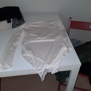 Vit långärmad bodysuit - Säljer en vit långärmad bodysuit med rund hals. Perfekt att styla med jeans eller kjol för en clean look. Materialet känns mjukt och stretchigt.