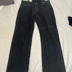 Svarta Levis 501 jeans - Klassiska svarta Levis 501 jeans med raka ben och femficksmodell. Jeansen har knappgylf och är tillverkade i kraftigt denimtyg. Perfekta för dig som gillar en tidlös och avslappnad stil.