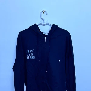 Svart hoodie från Lanvin x Gallery Dept. - Säljer en svart hoodie från Lanvin i samarbete med Gallery Dept. Tröjan har dragkedja, huva med snörning och tryck både fram och bak. Tillverkad i 100% bomull och har en avslappnad passform. Perfekt för dig som gillar streetwear.