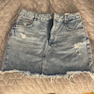 Ljusblå jeanskjol från Pull&Bear - Säljer en ljusblå jeanskjol från Pull&Bear med slitna detaljer och fransig nederkant. Säljer för att den inte kommer till användning. Storlek L men sitter som en lågmidjad S. Jättefint skick