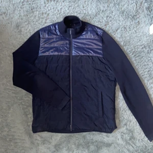 Cardigan från Massimo Dutti - Snygg marinblå jacka från Massimo Dutti med glansiga paneler upptill och ribbad krage. Jackan har dragkedja framtill och två fickor. 