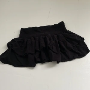 Svart volangkjol från SHEIN - Jättevacker svart kortkjol från SHEIN med bred resår i midjan och flera lager volanger. Kjolen är perfekt för dig som gillar en feminin och lekfull stil. Modellen är kort och passar till många olika looks.