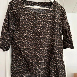 Leopardmönstrad topp från Isolde - Säljer en snygg topp från Isolde i leopardmönster med dragkedjedetalj framtill. Toppens färger går i svart och beige, och den har halv-långa ärmar. Perfekt för dig som gillar djurmönstrat och vill sticka ut lite extra.