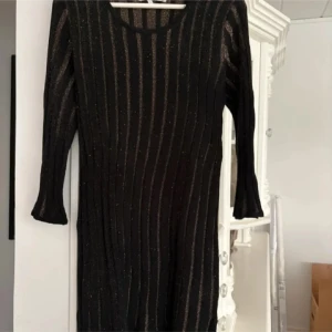 Svart glittrig klänning från Flash Woman - Säljer en svart glittrig klänning från Flash Woman i storlek L. Klänningen har lång ärm och ett ribbat, randigt mönster med glittriga detaljer. Perfekt för dig som vill sticka ut lite extra.