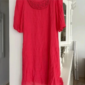 Röd klänning med pärldetaljer från Isay - Säljer en röd klänning från Isay med pärlade detaljer vid halsringningen. Klänningen har korta ärmar och är tillverkad i ett lätt, transparent material med ett innertyg. Perfekt för dig som gillar färg och vill sticka ut.