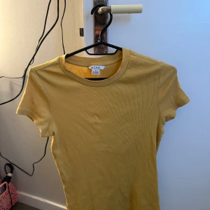 Gul ribbad t-shirt från Monki - Säljer en gul ribbad t-shirt från Monki med rund halsringning och korta ärmar. Perfekt för dig som gillar enkla och färgglada basplagg. Superfin att matcha med jeans eller kjol!