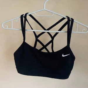 Svart sport-bh från Nike - Svart sport-bh från Nike med smala korsade axelband i ryggen och klassisk logga framtill. Perfekt för träning och ger bra stöd med sin tighta passform.
