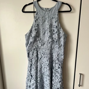 Ljusblå spetsklänning - Superfin ljusblå klänning med spetsdetaljer och ärmlös design. Klänningen har en rund halsringning och vackert blommigt mönster i spetsen. Perfekt för sommarens tillfällen eller studentfirande!