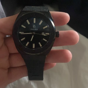 Svart klocka från Paul Rich - Stilren svart klocka från Paul Rich med svart urtavla och silverfärgade index. Klockan har datumvisning och svart länkarmband i rostfritt stål. Perfekt accessoar för dig som gillar en modern och minimalistisk look. Nypris 4000kr låda och allt följer med