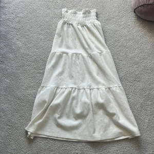 Vit långkjol med volang - Säljer en vit långkjol med bred resår i midjan och flera volanglager. Kjolen har en luftig och flowy känsla, perfekt för varma dagar. Enkel att matcha med olika toppar för en chill look.