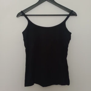 Svart linnetopp med smala axelband - En enkel och stilren svart linnetopp med smala axelband. Perfekt att matcha med jeans eller kjol för en clean look. Tunn och lätt, passar bra till varma dagar.