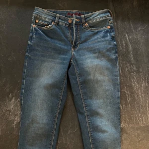 Blå jeans från Honey B Blue - Säljer ett par klassiska blå jeans från Honey B Blue med normal passform. Jeansen har fem fickor, orangea sömmar och stängs med knapp och dragkedja. Materialet är en mix av bomull och polyester för extra komfort. Storlek 34