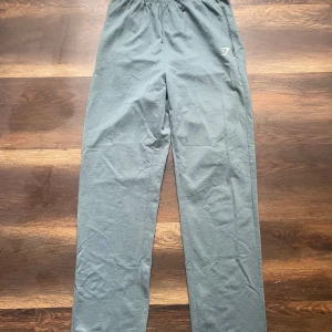 Grå träningsbyxor från Gymshark - Säljer ett par grå träningsbyxor från Gymshark med elastisk midja och dragkedjefickor. Byxorna har en avslappnad passform och är perfekta för gymmet eller andra sportaktiviteter.