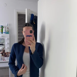 Mörkblå cardigan jacka från Moodo - Säljer en mörkblå cardigan jacka från Moodo i storlek XS. Jackan har lång ärm och ett diskret sicksackmönster i tyget. Modellen är öppen framtill utan knappar eller dragkedja och har en rak, enkel passform.