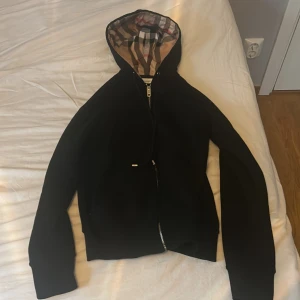 Svart Burberry hoodiejacka med rutig huva - Äkta burberry svart hoodie storlek smal till ungefär längd 175 minus är att vid 1 av fickorna så är den lite trasig men syns knappt 