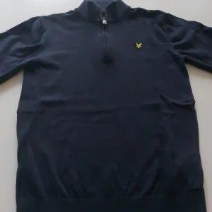 Mörkblå half zip tröja Lyle & Scott - Mörkblå långärmad tröja från Lyle & Scott med half zip och klassisk gul logga på bröstet. Tröjan har hög krage och är i mjukt material, perfekt för en chill och stilren look. Passar dig som gillar enkel men snygg design. Aldrig använd. Går att diskutera pris