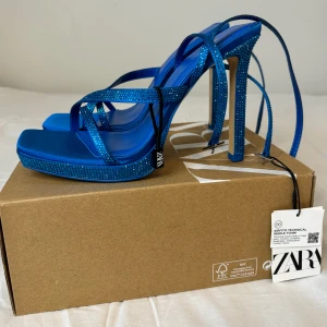 Blå glittriga platåsandaler från Zara - Säljer dessa helt nya blå klackar från Zara, aldrig använda och med tag kvar. Fantastiska detaljer med strass, ankelband och hög platå. Perfekta för fest, bröllop eller en utekväll.Köpt för 699kr säljer för 200kr. Helt oanvända kommer i orginalförpackning