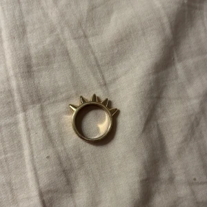 Guldig ring med spikes - Cool ring i guldton med fem spetsiga spikes på ovansidan. Ringen har en chunky känsla och ger en edgy vibe till din stil. Perfekt för dig som vill sticka ut och addera lite attityd till outfiten.