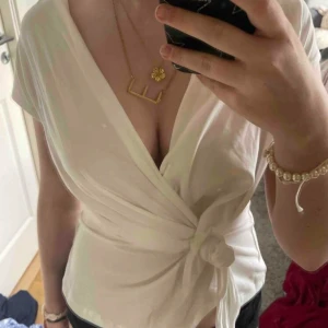 Vit omlottopp med knyt i midjan - Säljer en stilren vit omlottopp med knyt i midjan och v-ringad hals. Toppen har korta ärmar och är tillverkad i ett mjukt, lätt material som känns skönt mot huden. Perfekt för dig som gillar en enkel men snygg look med lite extra detalj vid midjan. Aldrig använd/utan prislapp