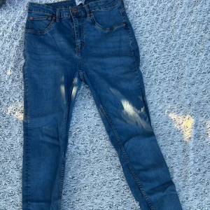 Blå jeans med raka ben - Säljer ett par klassiska blå jeans med raka ben och femficksmodell. Jeansen har normal passform, orangea sömmar och är tillverkade i jeansmaterial. Perfekta för en avslappnad stil och funkar året runt.