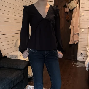 Svart blus med volang och v-ringning - Supersnygg svart blus från Gina tricot/ y-hill med v-ringning, volangdetaljer och prickig struktur i tyget. Långa ärmar med lätt puff vid axlarna. Helt ny, aldrig använd. Säljer den då den inte är min stil längre, lite liten också💕