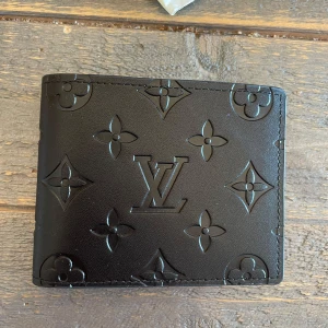 Svart plånbok  - Snygg svart plånbok monogrammönster i relief. Plånboken är tillverkad i exklusivt skinn och har flera kortfack och plats för sedlar. Perfekt accessoar för dig som gillar stilrena och lyxiga detaljer.