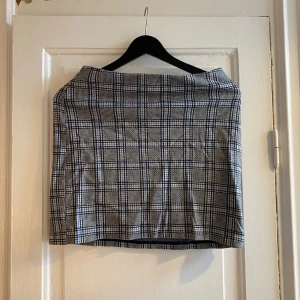 Rutig kjol - Snygg kortkjol med rutigt mönster i svart och vitt. Kjolen har rak passform och är perfekt för dig som gillar en klassisk men trendig stil. Materialet känns mjukt och följsamt, och kjolen är enkel att matcha med både t-shirt och stickad tröja.