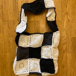Svartvit stickad axelväska - Helt ny virkad väska i ett schackrutigt mönster med svart/grå/ naturvit och vit färg. Väskan har ett virkat handtag i samma mönster. Mått: 25x25 x9 cm ﻿Axelrem: 65x9 cm  Inga bilder när den sitter på mig! Katter finns i hemmet!