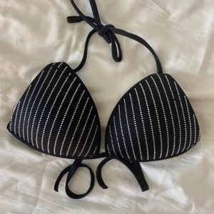 Svart bikiniöverdel från Calzedonia - Snygg svart bikiniöverdel från Calzedonia med tunna vita ränder av små glittriga stenar. Klassisk trekantsmodell med knyt i nacke och rygg. Tillverkad i stretchigt material som sitter skönt och formar sig efter kroppen. Perfekt för strandhäng och poolparty!