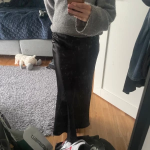 Svart långkjol i satin - Säljer en svart långkjol i glansigt satinmaterial. Kjolen har en rak och elegant passform, helt oanvänd med prislapp kvar!!