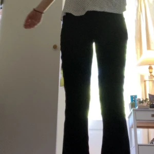 Svarta kostymbyxor med bootcut - Snygga svarta lågmidjade kostymbyxor. Byxorna har två knappar framtill, bälteshällor och fickor med knappdetalj bak. Perfekta för en clean och stilren look. Materialet känns mjukt och stretchigt för extra komfort.