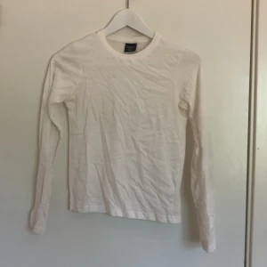 Vit långärmad basictröja barn - Enkel och stilren vit långärmad tröja från dollarstore i storlek 134/140. Tröjan har rund halsringning och är gjord i mjuk bomull, perfekt för lager-på-lager eller som den är. Passar dig som gillar en clean och klassisk look.