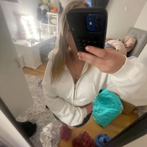 Vit croppad hoodie med dragkedja - Säljer en vit croppad hoodie med huva och dragkedja framtill. Tröjan har långa ärmar, ribbade muddar och två fickor framtill. Perfekt för en chill och avslappnad stil. Passformen är loose och materialet känns mjukt och skönt.